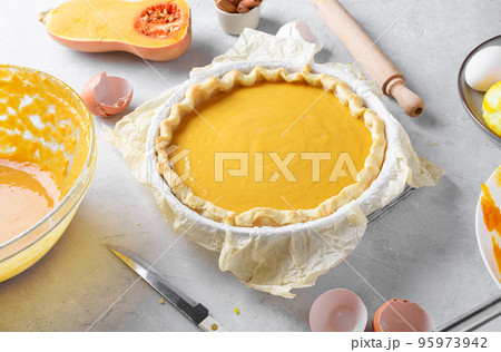 Uncooked pumpkin pie into a baking dish ready for cooking on a gray kitchen table surrounded by ingredients, close up 95973942