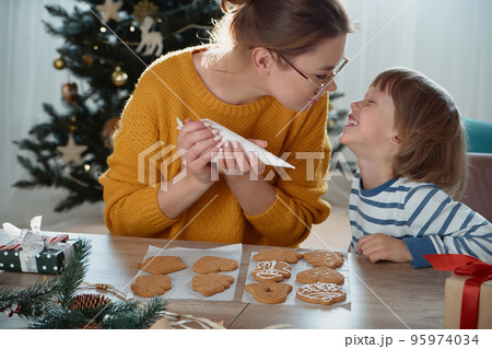 Mother and child decorating Christmas gingerbread cookies with sugar icing and having fun together Mother and child decorating Christmas gingerbread cookies with sugar icing and having fun together 95974034
