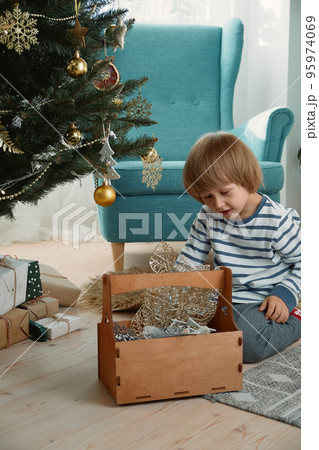 Child decorating a Christmas tree sitting in pajamas in a home interior 95974069