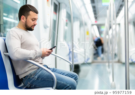 Young man using smartphone while traveling in subway car Young man using smartphone while traveling in subway car 95977159