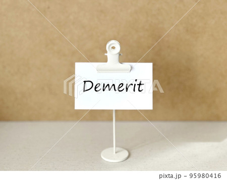 クリップスタンドとDemeritの文字入り白い紙_コルク背景 クリップスタンドとDemeritの文字入り白い紙_コルク背景 95980416
