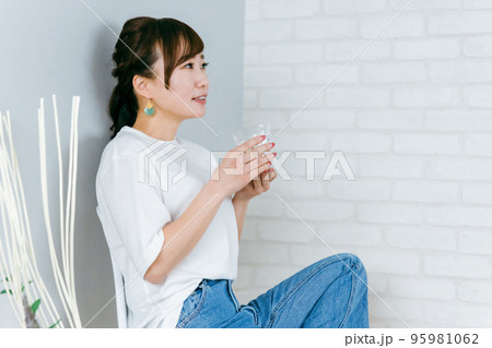 部屋で椅子に座りながらウォーターサーバーの水を飲むジーンズ姿のアジア人女性 95981062