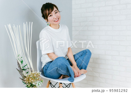 椅子の上で胡坐をかくジーンズ姿のおしゃれな日本人女性 95981292