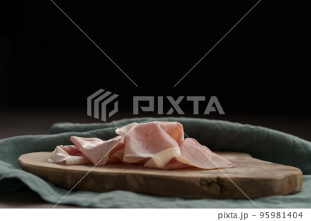 Thin slices of prosciutto cotto on olive wood board 95981404