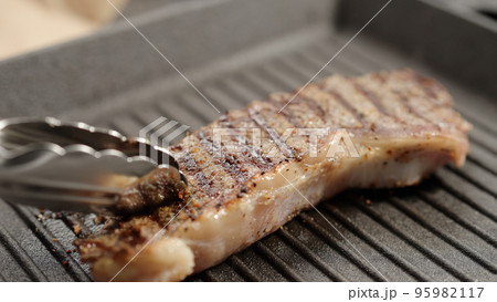 flip new york steak with tongs on grill pan 95982117