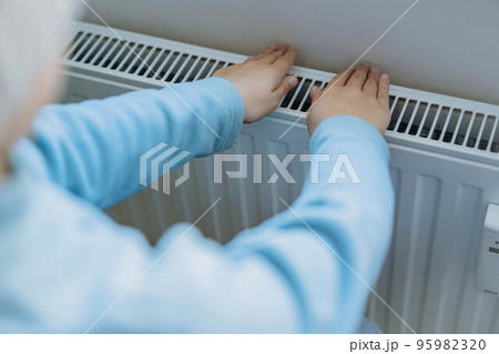 child warming hands over heater. Energy crisis in Europe 95982320