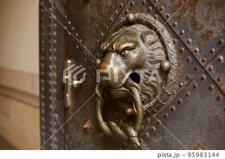 A door knocker in the shape of a lion adorns an old door 95983144