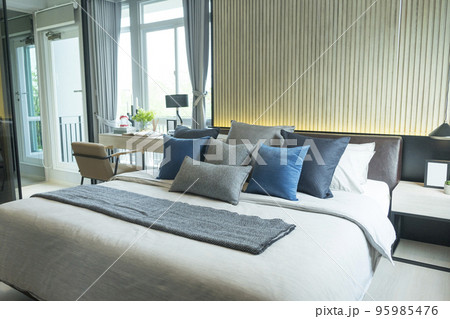 Blue pillow on king size bed in contemporary bedroom with modern lamp and vase on nightstand table. Blue pillow on king size bed in contemporary bedroom with modern lamp and vase on nightstand table. 95985476