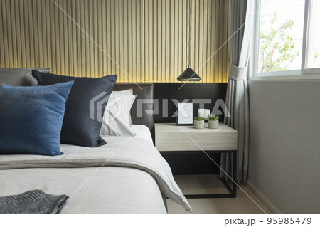 Blue pillow on king size bed in contemporary bedroom with modern lamp and vase on nightstand table. 95985479