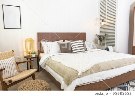 Stylish bedroom interior with wooden bed, furniture, flowers in vase, rattan decoration and elegant accessories. Beautiful bed sheets, blanket and pillows. Cozy home decor. Stylish bedroom interior with wooden bed, furniture, flowers in vase, rattan decoration and elegant accessories. Beautiful bed sheets, blanket and pillows. Cozy home decor. 95985652