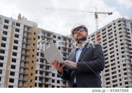 Bearded building inspector making notes on laptop at construction site Bearded building inspector making notes on laptop at construction site 95987666