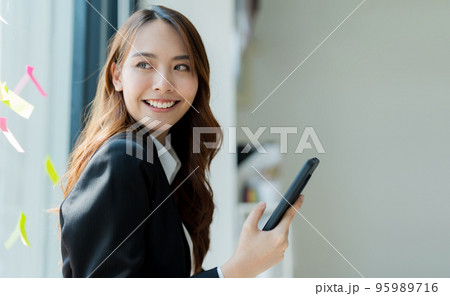 Happy young asian business woman wearing suit holding mobile phone 95989716