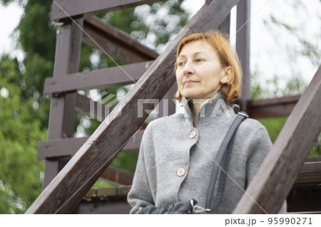 A red hair woman in the grey jacket sits in the city park A red hair woman in the grey jacket sits in the city park 95990271