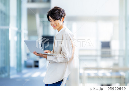 オフィスのロビーでノートパソコンを持って立っている若い男性 95990649