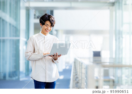 オフィスのロビーでノートパソコンを持って立っている若い男性 95990651