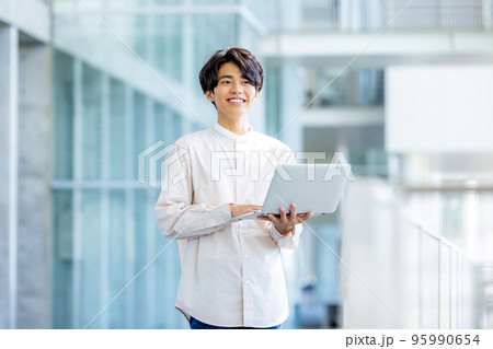 オフィスのロビーでノートパソコンを持って立っている若い男性 95990654