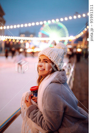 Smiling woman in winter style clothes with coffee near skating rink. Young woman enjoying winter holidays. Smiling woman in winter style clothes with coffee near skating rink. Young woman enjoying winter holidays. 95991311