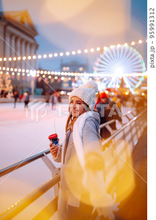 Smiling woman in winter style clothes with coffee near skating rink. Young woman enjoying winter holidays. Smiling woman in winter style clothes with coffee near skating rink. Young woman enjoying winter holidays. 95991312