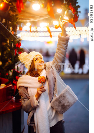 Young woman with caramel apple on Christmas market. Smiling woman in winter style clothes posing. Young woman with caramel apple on Christmas market. Smiling woman in winter style clothes posing. 95991392