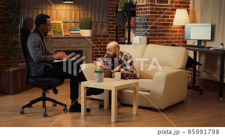 Man talking about conflict at counseling session with therapist in office, laying on couch and complaining about problems. Asking for professional assistance and help at appointment. Man talking about conflict at counseling session with therapist in office, laying on couch and complaining about problems. Asking for professional assistance and help at appointment. 95991798