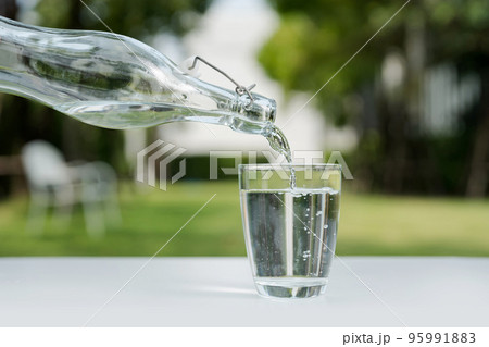 Pour the water from the water bottle into the glass. Pour the water from the water bottle into the glass. 95991883