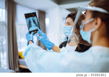 A female doctor in visor and protective gloves discussing an x-ray. Doctor examines an X-ray. A female doctor in visor and protective gloves discussing an x-ray. Doctor examines an X-ray. 95992901