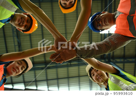 Smiling warehouse workers team stacking hands together bottom view. Unity, supporting and teamwork concept 95993610