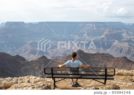 Rear View Of Man Sitting On Bench And Exploring Majestic Grand Canyon National Park and Cloudy Sky In Arizona During Summer Rear View Of Man Sitting On Bench And Exploring Majestic Grand Canyon National Park and Cloudy Sky In Arizona During Summer 95994248