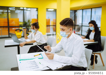 Office worker wearing face mask for social distancing for virus prevention while using laptop. 95994651
