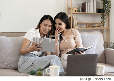 Happy two young asian girls are sitting on couch using digital tablet at home Happy two young asian girls are sitting on couch using digital tablet at home 95994726