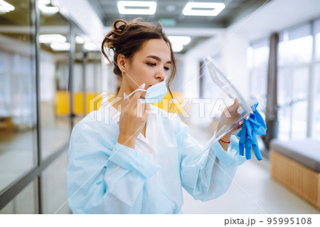 Young Nurse take off protection mask and visor after a work day. Disease control expert at office. 95995108