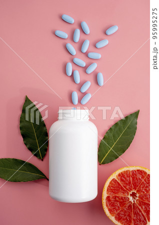 Natural food supplements pills, white plastic bottle with vitamins, pink background and sun light with shadows. Natural food supplements pills, white plastic bottle with vitamins, pink background and sun light with shadows. 95995275