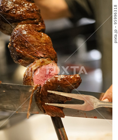 Picanha is a BBQ Steak meat grilled in charcoal. Knife cutting on skewer. Brazilian meat in a Churrascaria restaurant Picanha is a BBQ Steak meat grilled in charcoal. Knife cutting on skewer. Brazilian meat in a Churrascaria restaurant 95996318