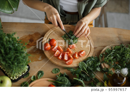 High angle view of hands of woman chopping arugula leaves, sitting at table in bright exotic studio 95997657