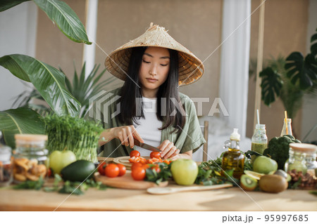 Young asian woman blogger or content creator choping tomatoes preparing vegan salad Young asian woman blogger or content creator choping tomatoes preparing vegan salad 95997685