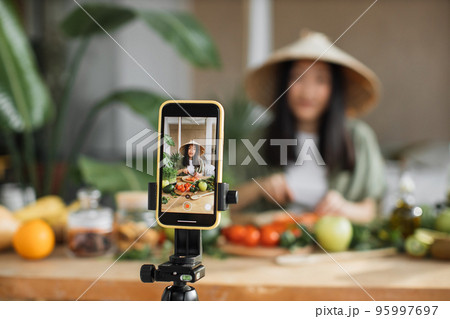 Young asian woman blogger or content creator chopping tomatoes preparing vegan salad Young asian woman blogger or content creator chopping tomatoes preparing vegan salad 95997697