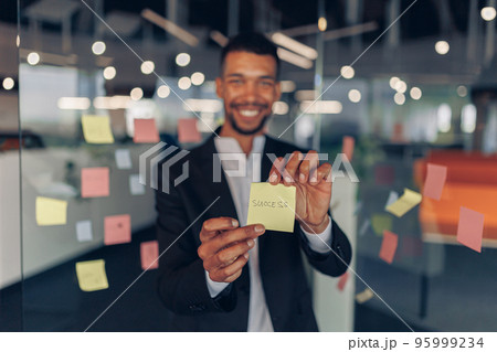 African Businessman showing sticky notes with motivational phrases while standing in office 95999234