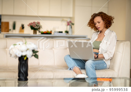 Ginger young woman sitting in the kitchen and working on a laptop 95999538
