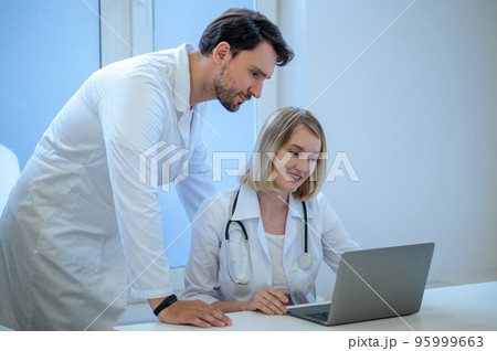 Two people in lab coats discussing something and looking interested Two people in lab coats discussing something and looking interested 95999663