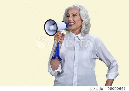Portrait of happy senior woman with megaphone. Isolated on yellow. 96000661