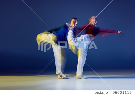 Portrait of young man and woman dancing isolated over dark blue background with mixed lights. Hip-hop synchronization Portrait of young man and woman dancing isolated over dark blue background with mixed lights. Hip-hop synchronization 96001119
