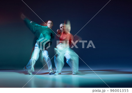 Portrait of young man and woman dancing contemp isolated over dark blue background with mixed lights. Red and green outfits 96001355