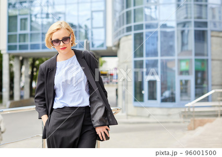 Beautiful blonde young woman wearing suit and walking on the street. A woman dressed in a business style walks around the city 96001500