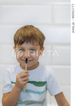 cute 5 years old boy brushing teeth with bamboo tooth brush with black bristles in bathroom. 96002777