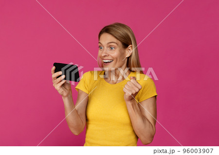 Surprised happy adult european lady with smartphone rejoices to victory, makes success gesture with hand 96003907