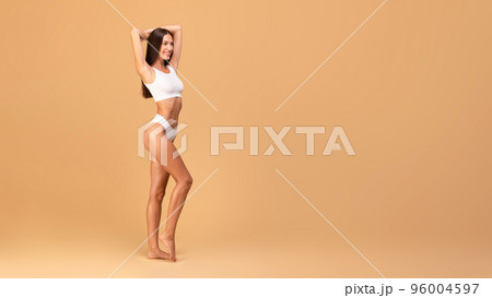 Young slender caucasian lady with perfect body shape posing in white lingerie, beige background, panorama, free space Young slender caucasian lady with perfect body shape posing in white lingerie, beige background, panorama, free space 96004597