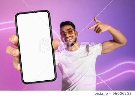 Cheerful arab guy in sunglasses pointing at modern cell phone Cheerful arab guy in sunglasses pointing at modern cell phone 96006252