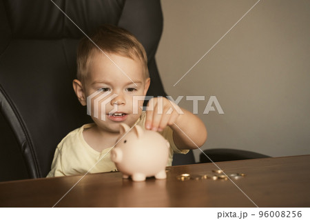 Child puts coins in piggy bank. Smart happy boy saving money in a piggy bank, learning about saving 96008256