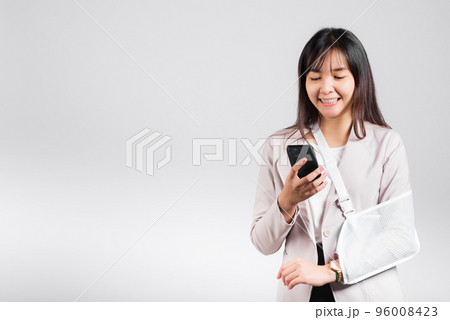 Woman confident smiling broken arm after accident and wear arm splint for treatment and hold smartphone, happy Asian female sling supported hand isolated on white background, social media, copy space 96008423