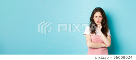 Thoughtful young teenage girl making assumption, look determined and pensive, planning something, staring at camera and thinking, standing over blue background Thoughtful young teenage girl making assumption, look determined and pensive, planning something, staring at camera and thinking, standing over blue background 96009024